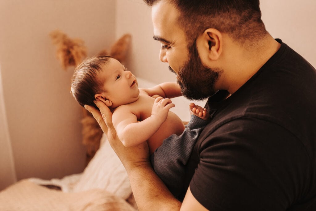 Newborn Photographer, a young father holds his newborn child in the home nursery
