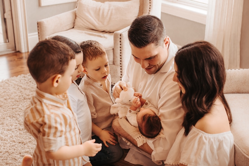 Newborn Photographer, a dad holds his newborn child as mom and young siblings look on in admiration